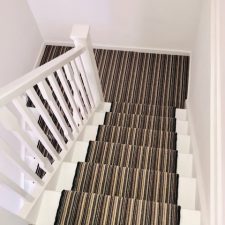 Earth stripe carpet by Hugh Mackay, view down stairs, with a black whipped edge runner to the steps.