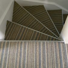 View down stairs fitted with striped carpet with door bars on the front of the steps.
