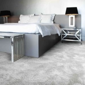 A bedroom featuring a double bed with white linen, a metal bedside table with lamp and thick grey carpet.