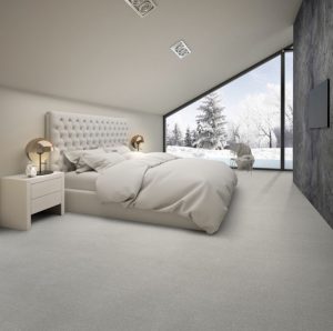 A bedroom with angled ceiling, with a super king size bed, grey duvet, grey carpet and view out onto snow.