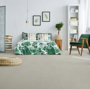 A bedroom with double bed and green flowery duvet, light grey walls and neutral carpet