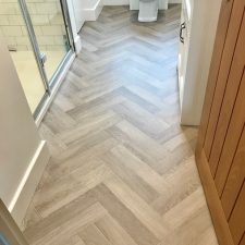 View of a bathroom floor fitted with a herringbone wood-effect vinyl flooring by Leoline from their Timberline range in Marilyn.