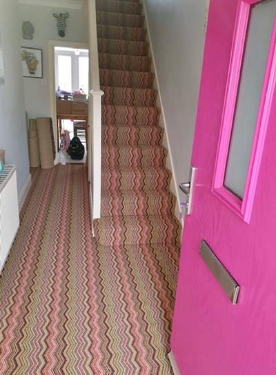 View of an open bright pink front door into a hallway fitted with a zig zag stripy carpet by Hugh Mackay from their deco collection in Notting Hill