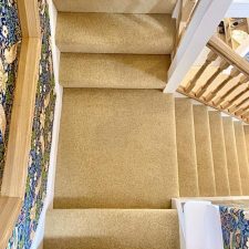 View down stairs from a landing fitted with a light brown woven Wilton carpet in 80% wool and 20% nylon pile. Extra heavy domestic quality, moth proofed.