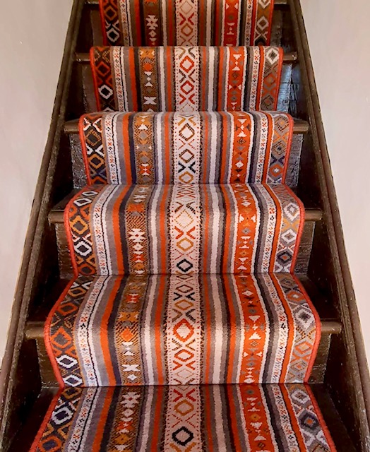 View of stairs fitted with a stripy, patterned wool Axminster carpet runner from the Quirky Stair Runners range in Tribe Passion.