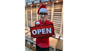 Carpet fitter Samuel Sargeant holding an 'open' sign and wearing a Santa hat in the Sargeant Carpets showroom