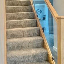 A flight of stairs with wooden balustrade fitted with a grey Saxony, extra heavy domestic beige carpet by Associated Weavers.