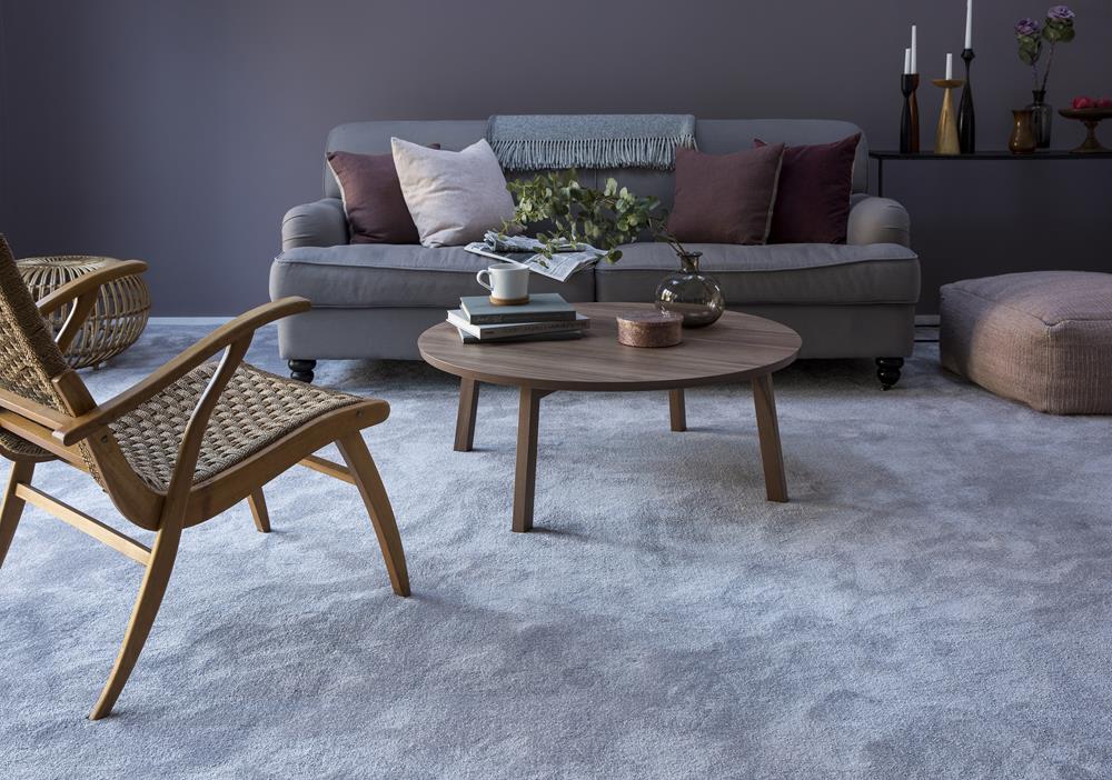 A living room with dark grey painted wall, grey sofa, wooden chair and table on a lush grey carpet from the Gemini range in Pennine Mist