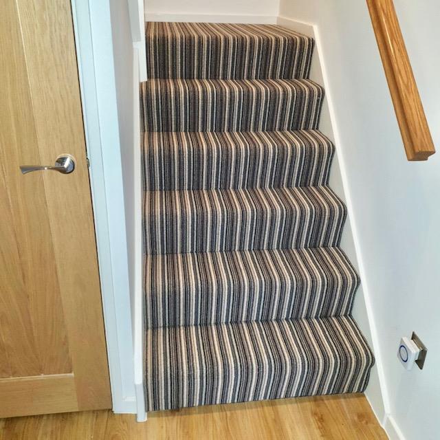 View of the bottom of a flight of stairs fitted with a 3 ply British wool heavy domestic brown stripy carpet from the Hugh Mackay range.