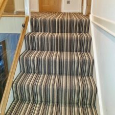View of a top of a flight of stairs and landing fitted with a 3 ply British wool heavy domestic brown stripy carpet from the Hugh Mackay range.