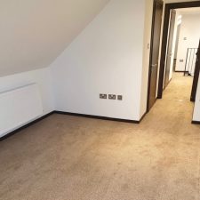 Room with a sloped ceiling and white walls fitted with a beige domestic polypropylene twist pile carpet.
