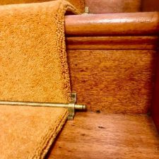 Closeup view of a wooden stair tread fitted with gold coloured wool/nylon pile moth proof carpet runner.