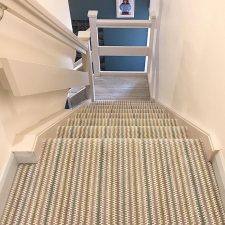 View down a staircase which is covered with a velvet tufted carpet in a neutral striped colour
