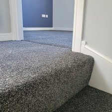 View of the top of a flight of stairs fitted with a dark grey polypropylene, bleach cleanable, heavy domestic carpet.