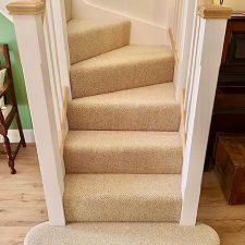 View of the bottom section of a flight of stairs fitted with a warm honey coloured wool loop, moth resistant carpet.