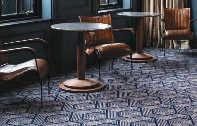 A geometric patterned carpet from the Vescent range shown in a hotel bar with tables and chairs