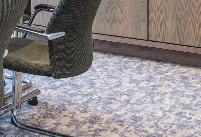 A patterned carpet in blues and neutrals shown with a chair and sideboard