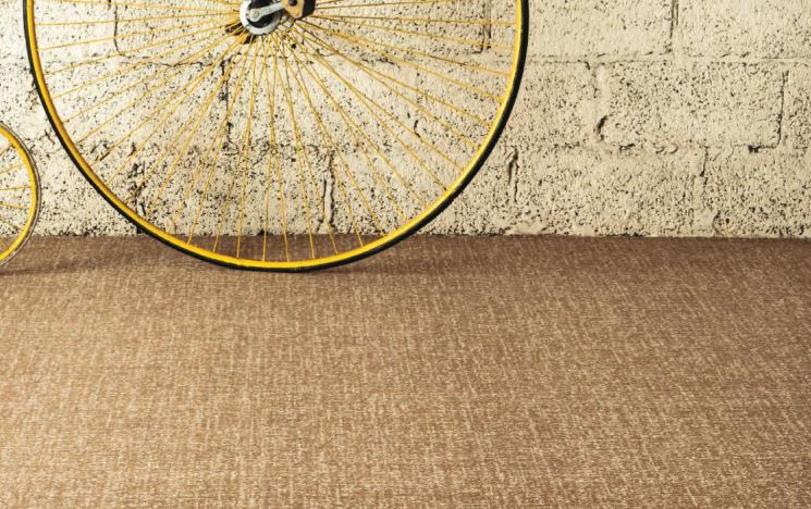 A yellow penny farthing in the background with a brown carpet from the Vescent range by Ulster Carpets