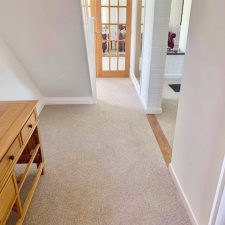 View of a hallway fitted with a neutral light brown wool berber twist carpet.