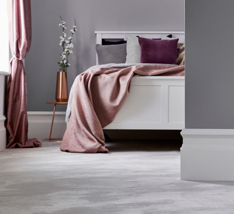 A bedroom with a white bed frame, bedside table and pink curtains, fitted with a grey Silken Velvet from Westex Carpet.