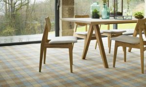 A dining table and chairs in a bright living room with a checked carpet from the Abbotsford range by Brintons.