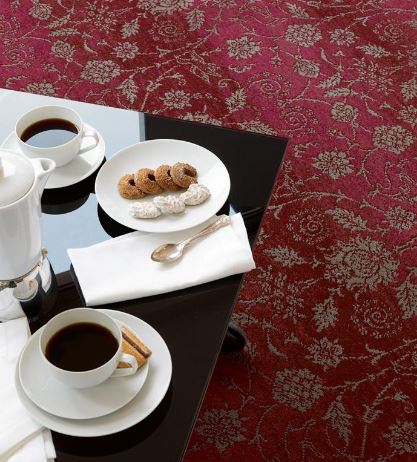 A deep red, patterned living room carpet from the Renaissance Classics range by Brintons.  Shown under a coffee table laid with two cups of coffee and a plate of biscuits.