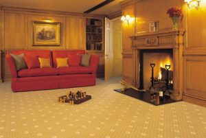 A cosy living room with red sofa and fireplace with a golden patterned carpet from the Royal Marquis range by Brintons.