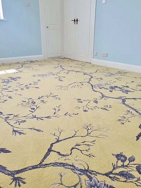 A blue patterned Axminster carpet on a pale yellow background fitted in a bedroom.