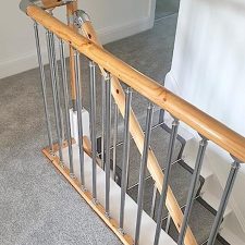 View of landing and through balustrade of stairs fitted with grey polypropylene carpet. The stairs have a 50mm darker grey linen binding to the stair runner and chrome effect solid stair rods.