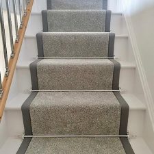View up a flight of stairs fitted with grey fade resistant, moth proof carpet. The stairs have a 50mm darker grey linen binding to the stair runner and chrome effect solid stair rods.