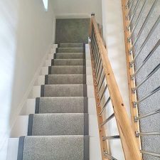 View down stairs fitted with grey twist pile carpet. The stairs have a 50mm darker grey linen binding to the stair runner and chrome effect solid stair rods.