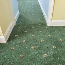 View of a corridor fitted with a green patterned, heavy wear, woven Axminster carpet.
