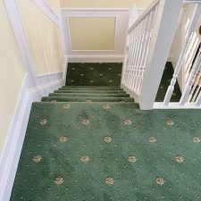 View down a flight of stairs fitted with a green patterned, heavy wear, woven Axminster carpet.