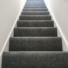 View down a flight of stairs fitted with a dark grey heavy domestic carpet.