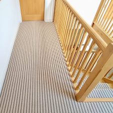 View of landing and stairs fitted with a neutral striped runner carpet with wooden treads. Carpet is made from British wool and is heavy domestic.