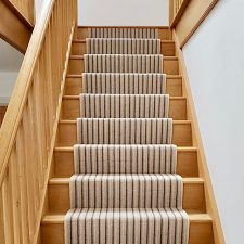 View down stairs fitted with a neutral striped runner carpet with wooden treads. Carpet is made from British wool and is moth resistent.