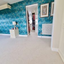 A bedroom with patterned blue wallpaper and neutral 80% wool, 20% nylon twist carpet which is made from 2 ply yarn, allergy guard treated, moth guard treated, and stain-resist treated.