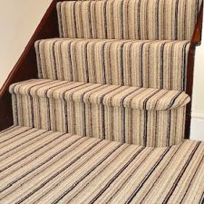 View of hall and stairs fitted with a striped loop pile carpet in shades of brown and beige.