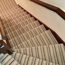 View down a flight of stairs fitted with a striped loop pile carpet in shades of brown and beige.