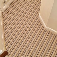 View of hall and stairs fitted with a striped loop pile carpet in shades of brown and beige.