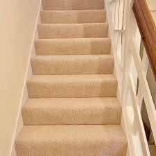 View up a flight of stairs fitted with a light beige berber twist pile heavy domestic carpet.