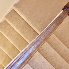 View of a flight of stairs fitted with a light beige berber twist pile heavy domestic carpet.