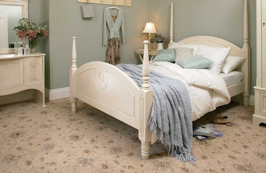 A bedroom with a cream coloured bed and furniture with patterned beige carpet