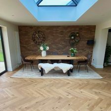 Large family room with vaulted ceiling with wooden floor and dining table over a bespoke woven axminster rug