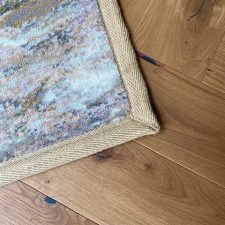 Closeup view of woven axminster rug with herringbone edge binding in light beige