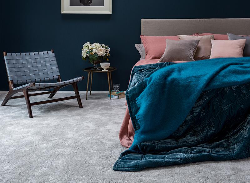 A bedoom with pink and blue soft furnishings, dark blue walls and grey carpet