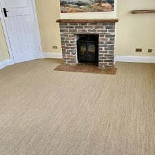 A living room with brick fireplace fitted with a neutral sisal carpet.