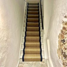 View up a flight of stairs fitted with a natural sisal herringbone runner with a cotton herringbone Oxford blue 1071 binding