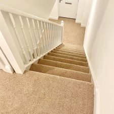 View down a flight of stairs fitted with a beige 80% wool berber twist pile heavy domestic carpet
