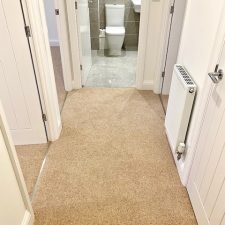 View of a hallway fitted with a plain beige 80% wool berber twist pile heavy domestic carpet